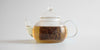 Side view of a glass teapot with tea inside, showing the glass infuser with small slits to allow water through.