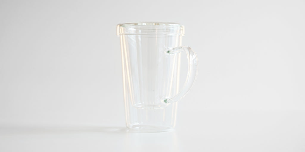 Rear view of the glass infuser cup, showing the handle. The infuser is in the cup, and the lid covers it.