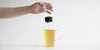 Side view of a glass cup filled with tea. A hand is removing the glass strainer, allowing the remaining tea to flow out of the slits in the infuser.