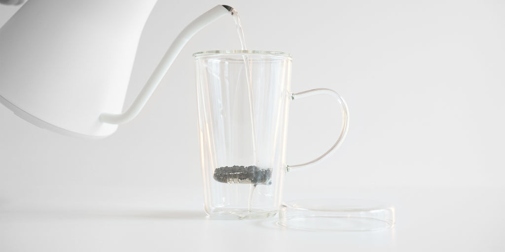 Side view of a glass cup with a glass infuser basket. The lid is off to the side, underneath the handle.