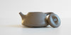 Side view of a gray duanni yixing teapot, with the lid facing the camera resting against the handle.