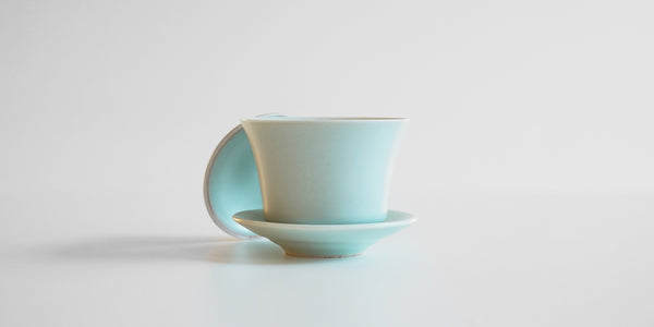 Side view of a blue-green celadon gaiwan. The lid is off, resting behind the bowl.
