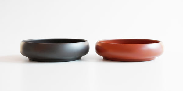 Two tea trays side by side, a black one on the left and a terracotta-colored one on the right.