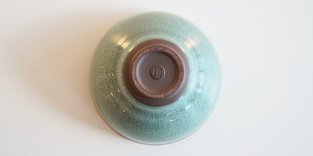 The bottom of a Longquan-style celadon bowl, with faint craquelure patterns and tiny white dots. Xu Chun Tian's maker's mark is stamped into the unglazed foot.