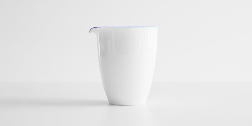 A tall white porcelain server, with a blue ring painted around the top edge and lip of the spout.