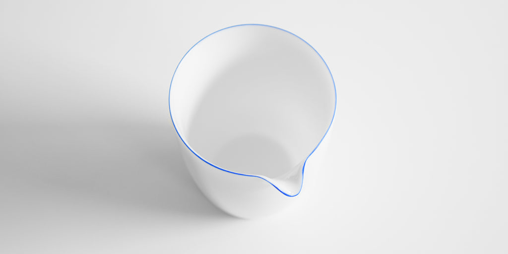 Close up of the inside of a white porcelain server, with a blue ring painted around the edge. The blue ring follows the top edge of the spout.