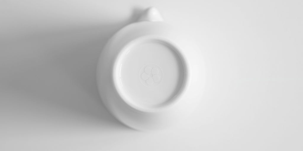 Close up of the bottom of a white porcelain server. Red Blossom Tea Company's logo is etched into the base.