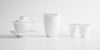 A set of matching white porcelain teaware with blue rings around the lips. From left to right, a gaiwan, a server, and two teacups.