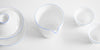 Close up of the top of a white porcelain server with a blue ring painted around the lip. A matching gaiwan is on the left, and a pair of matching cups on the right.