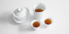 A collection of matching teaware, white porcelain with a blue ring painted around the edge of each piece. A gaiwan on the left, server in the top right, and two cups in the bottom right. The server and cups are filled with tea.