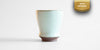Side view of a small blue-green celadon drinking cup in a shape similar to a tulip glass. A gold ribbon in the top right corner reads "New Arrival"