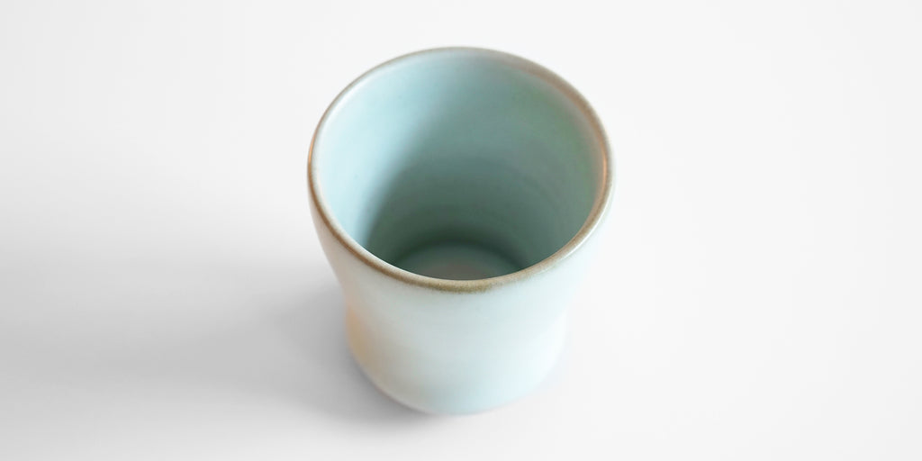 Top view of the inside of a blue-green celadon drinking cup. The thin edge is light brown in color.