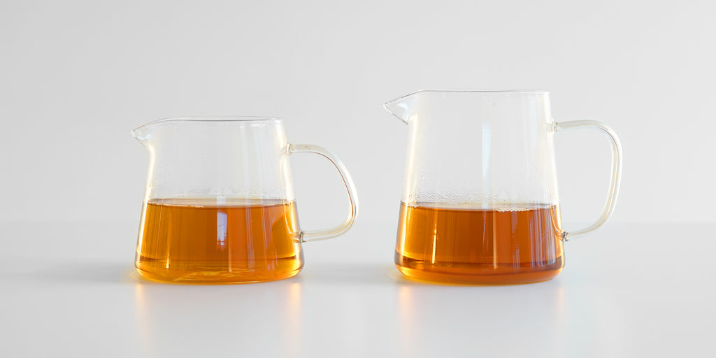 Two glass servers side by side with tea in them, a smaller one on the left, larger on the right.