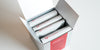 A silver box with 4 white bags of tea showing the Red Blossom Tea Company logo inside.