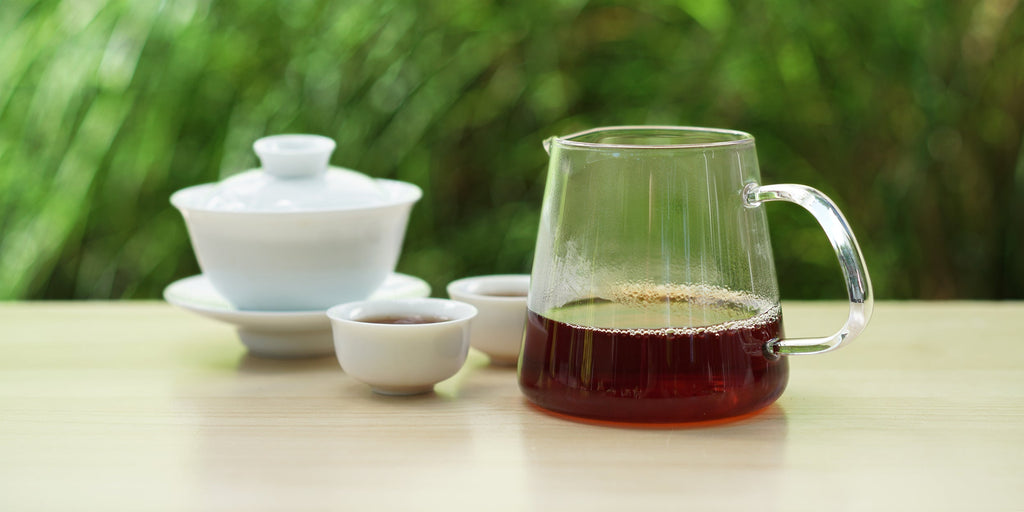 From left to right, a gaiwan, two teacups, and a glass server. The teacups and server have black tea in them.