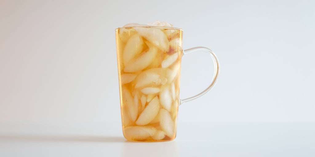 A side view of a glass cup filled with ice and black tea on a white background.