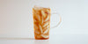 A glass cup filled with ice and lychee-scented black tea on a white background.