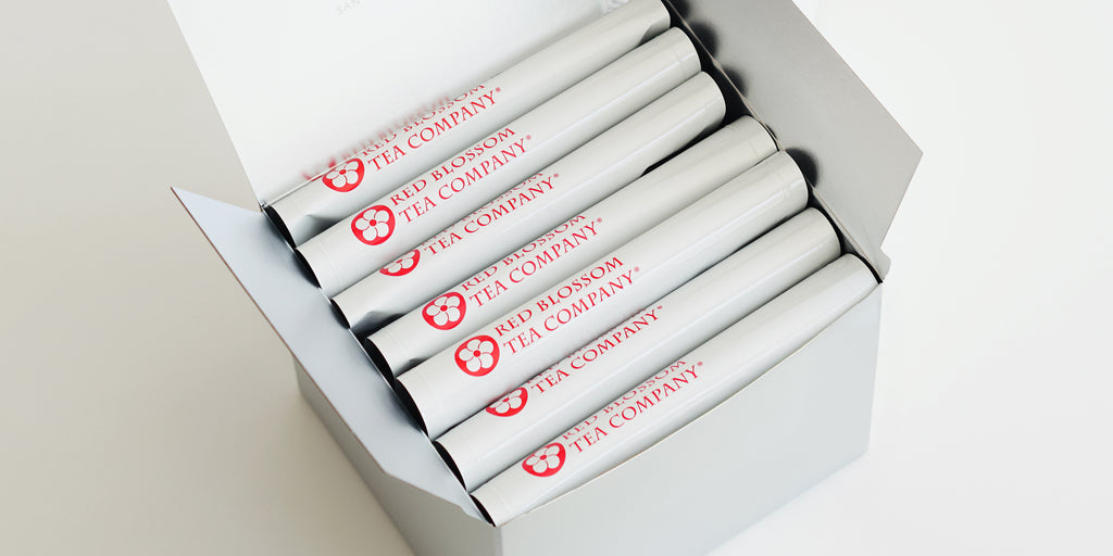 A silver box with 7 white bags of tea showing the Red Blossom Tea Company logo inside.