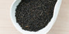 A white dish containing dry black tea leaves.