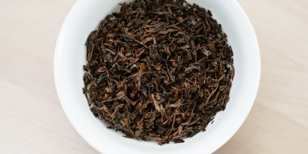 A white dish containing dry black tea leaves.