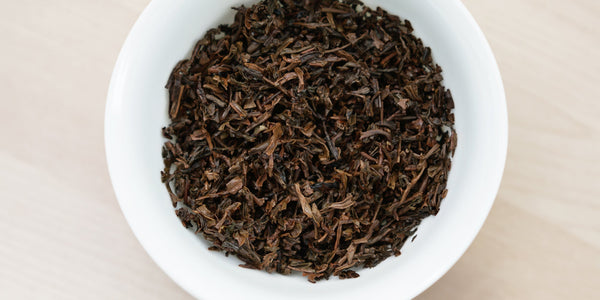 A white dish containing dry black tea leaves.