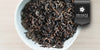 A white dish containing dry aged tea leaves and small orchid flowers. A black ribbon in the top right corner reads “Private Collection”