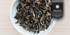 A white dish containing dry aged Tieguanyin tea leaves. A black ribbon in the top right corner reads “Private Collection”