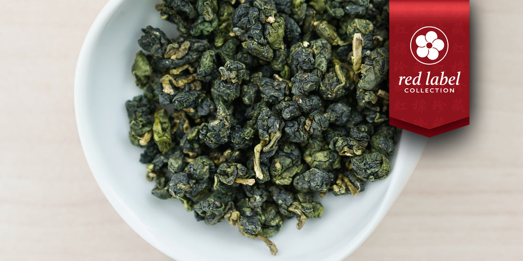 A white dish containing dry Formosa oolong tea leaves. A red ribbon in the top right corner reads “Red Label Collection”