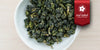 A white dish containing dry Formosa oolong tea leaves. A red ribbon in the top right corner reads “Red Label Collection”