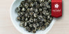 A white dish containing dry ball-rolled jasmine tea leaves. A red ribbon in the top right corner reads “Red Label Collection”