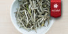 A white dish containing dry white tea leaves. A red ribbon in the top right corner reads “Red Label Collection”