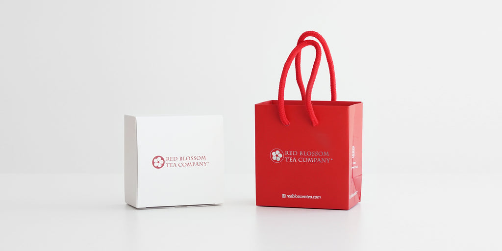 A small white box with a red logo on it next to a small red bag with a silver logo.