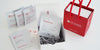 A white gift box containing 4 sample packs of tea and a pack of tea sachets to brew them with. On the right, another box is inside a small branded red bag.