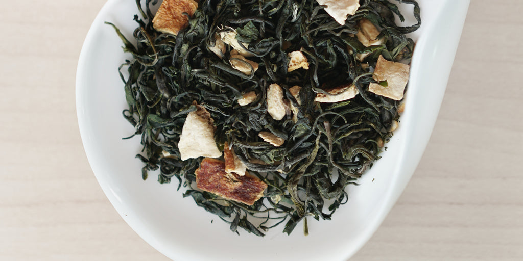 A white dish containing dry green tea leaves, dried orange peel, and ginger.
