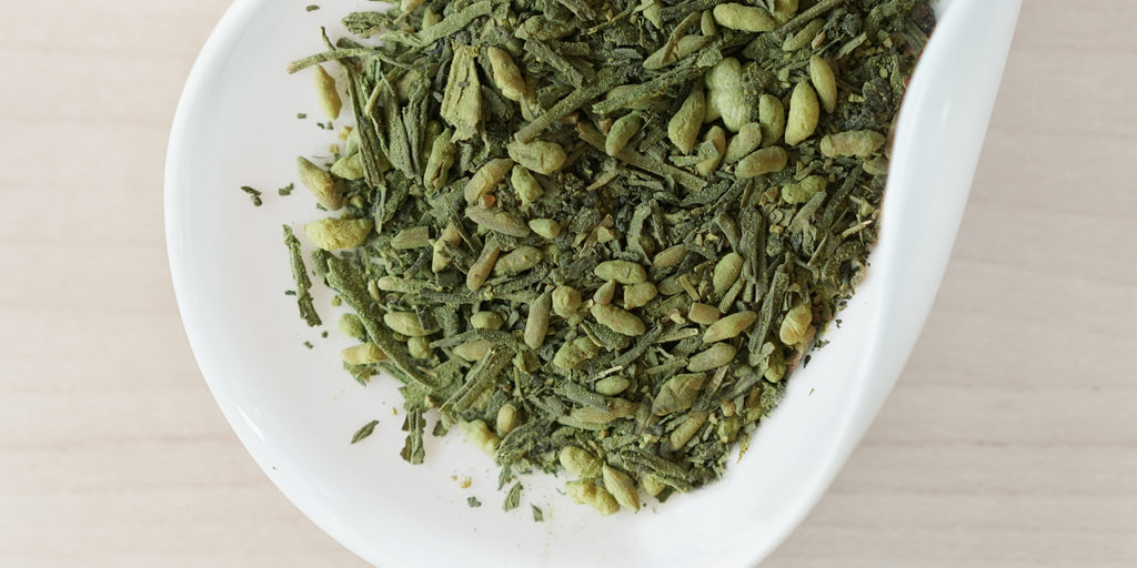 A white dish containing dry green tea leaves, toasted rice, and matcha powder.