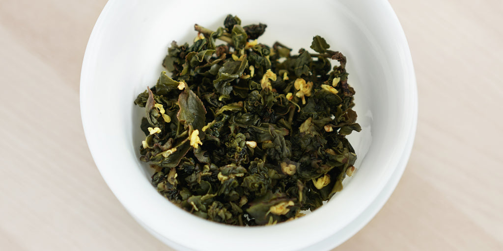 A top-down photo of brewed Formosa oolong tea leaves and yellow osmanthus flowers in a gaiwan.