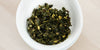 A top-down photo of brewed Formosa oolong tea leaves and yellow osmanthus flowers in a gaiwan.