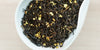 A white dish containing dry black tea leaves mixed with yellow osmanthus flowers.