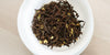 A top-down photo of brewed black tea leaves and yellow osmanthus flowers in a gaiwan.