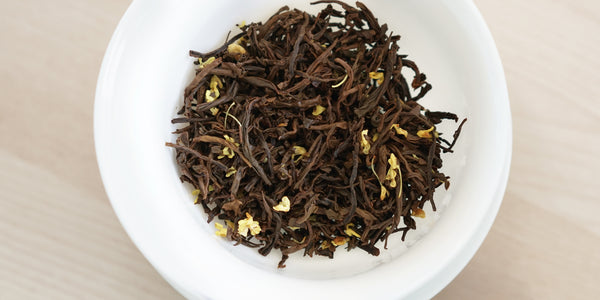 A top-down photo of brewed black tea leaves and yellow osmanthus flowers in a gaiwan.