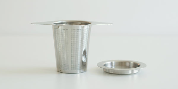 Side view of a steel infuser basket, with wings to hang over the top of a cup. A steel lid is set off to the side.