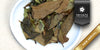 A white dish containing dry aged white tea leaves. A black ribbon in the top right corner reads “Private Collection", and a gold ribbon in the bottom right corner reads “New Arrival”