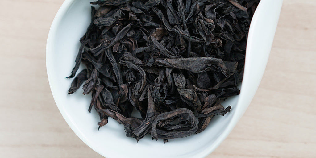 A white dish containing dry Wuyi oolong tea leaves.