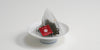 A triangular tea bag with a red label sits on a small white dish.