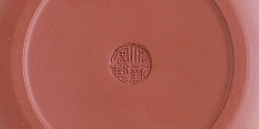 The bottom of a terracotta-colored yixing teapot. A maker’s mark is stamped into the base.