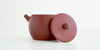 Side view of a terracotta-colored yixing teapot. The lid is facing the camera, resting against the handle.