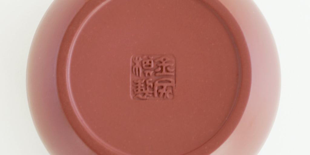The bottom of a terracotta-colored yixing teapot. A maker’s mark is stamped into the base.