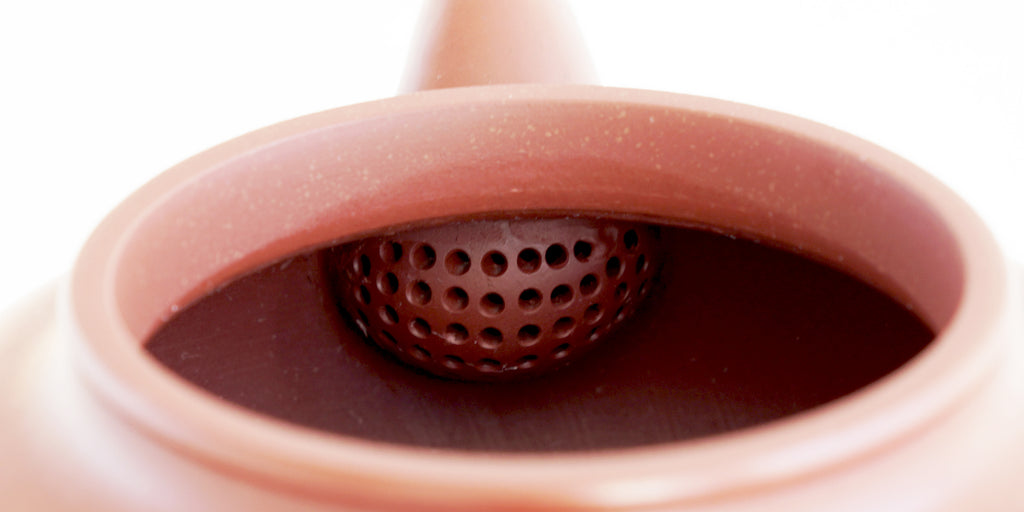 Rear view of the inside of a terracotta-colored yixing pot, showcasing the built-in filter made by punching small holes in the clay.