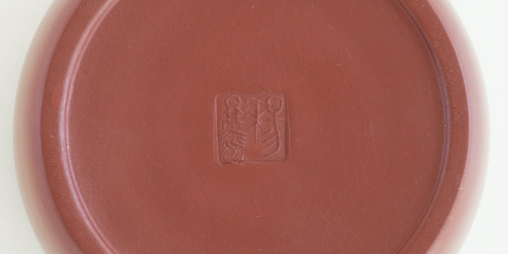The bottom of a terracotta-colored yixing teapot. A maker’s mark is stamped into the base.