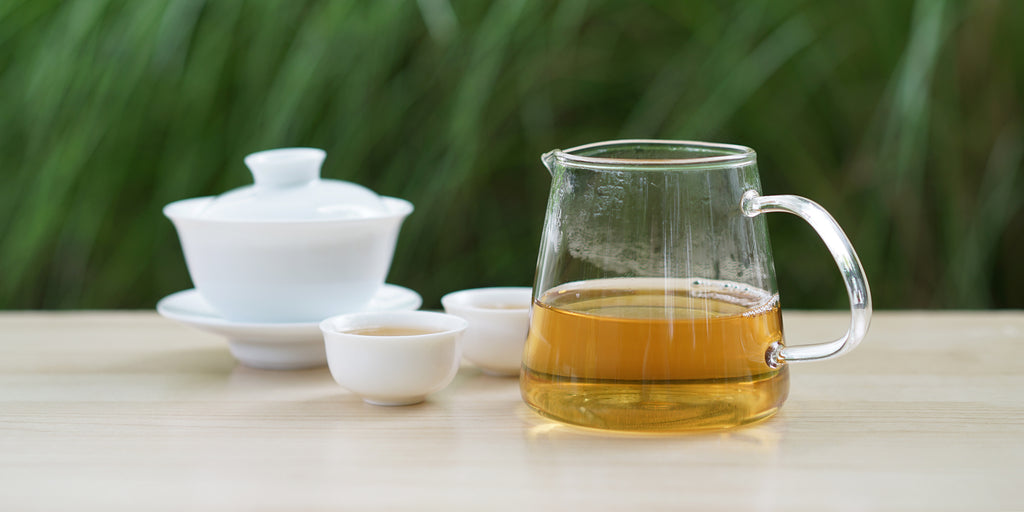 From left to right, a gaiwan, two teacups, and a glass server. The teacups and server have Tieguanyin tea in them.